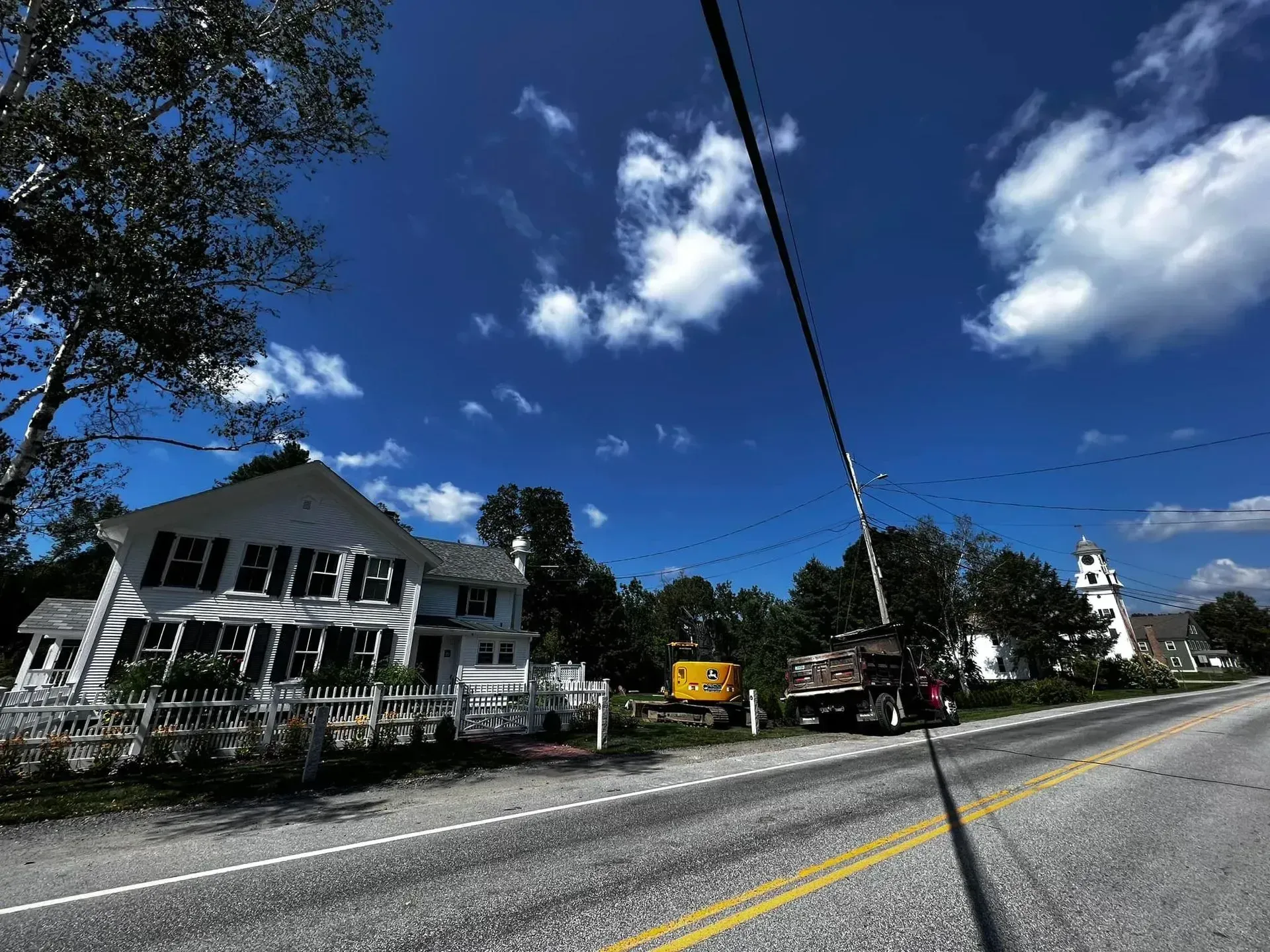 Roadside excavation job with a dump truck near a historic white colonial home