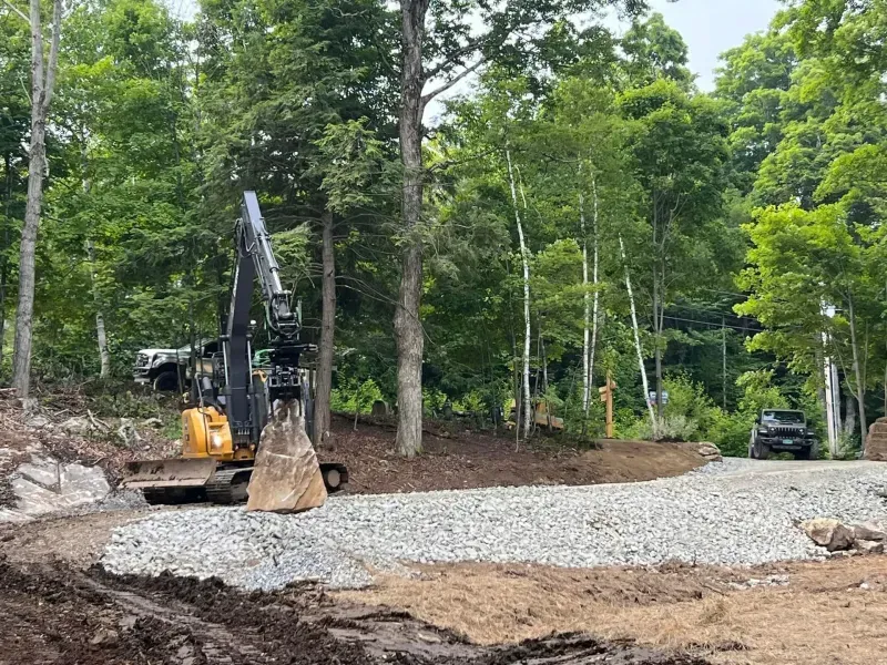 Excavator with a tilt-rotator spreading crushed gravel for a driveway